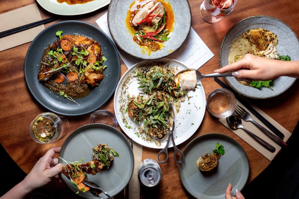 Shared Asian-fusion feast at Gwylo Mollymook with hands reaching for Babi Guling and prawn dumplings.