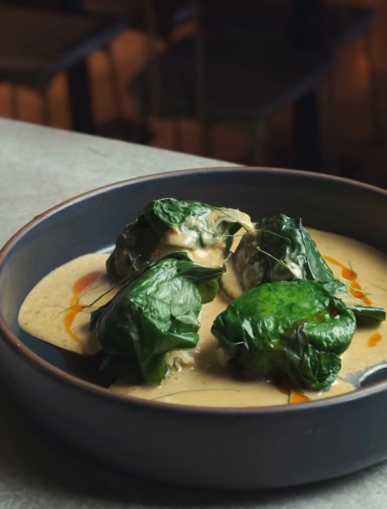 Prawn and scallop dumplings wrapped in green betel leaves in red curry sauce on a table at Gwylo.
